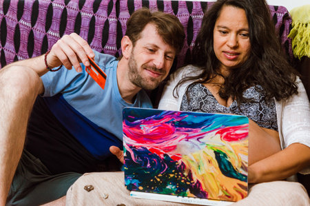 front view of latin adult couple of man and pregnant woman watching the laptop while shopping online, sitting on the sofa.の写真素材