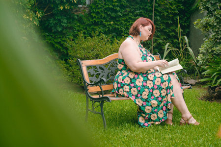beautiful latin young woman reading a book in the garden, plus size model, enjoying the weekend relaxing in the backyard home. copy space.の写真素材