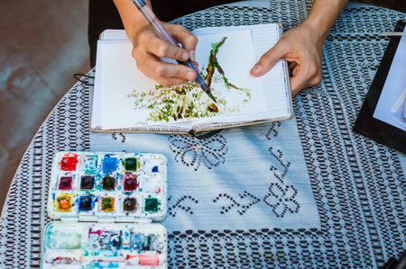 unrecognizable female caucasian hands, creating a drawing, painting on a notebook with watercolors...