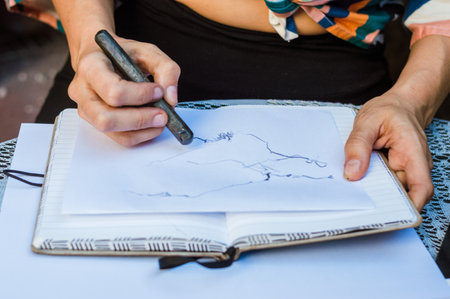closeup of unrecognizable caucasian woman sitting outdoors, drawing on a paper on a notebook with graphite, concept art, copy space.の写真素材