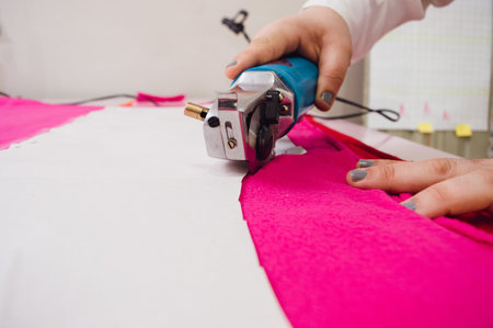 closeup female hands using of mechanical fabric cutter cutting fuchsia fabric, working from atelier at home, copy space, sewing and cutting conceptの写真素材