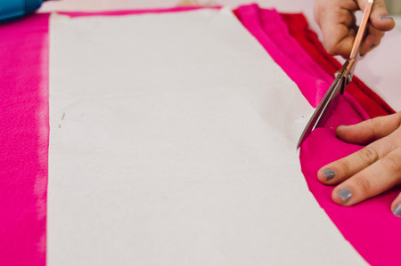 unrecognizable female caucasian hands cutting fuchsia fabric with scissors, on a table in a cut and sew workshop.の写真素材
