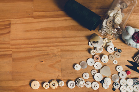top view of plastic buttons with a roll of thread and other textile implements placed on a wooden table with copy space.の写真素材