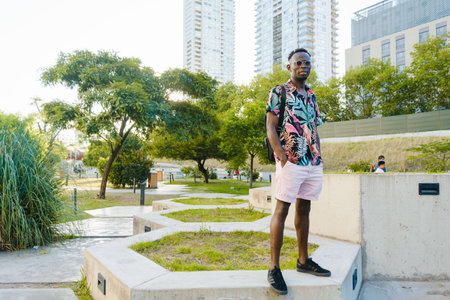 young man of african ethnicity, standing in the college garden, hands in pocket, waiting for his...