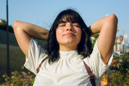 break from long class at university, young woman outdoors, sitting with arms behind head and eyes closed, relaxed and breathing.の写真素材