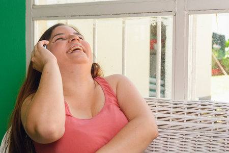 young latin argentinian woman at home happy sitting laughing out loud while talking on the phone, technology concept, copy space.の写真素材