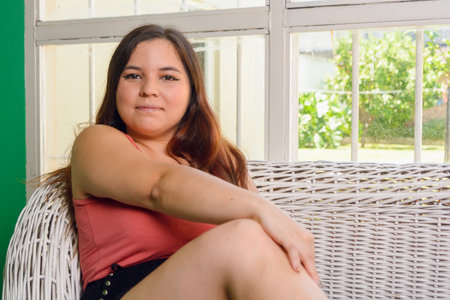 Tranquility and peace at home, portrait of young Latina woman, of Argentinian ethnicity, with comfortable clothes, long hair and white leather, relaxed sitting at home looking at the camera.の写真素材