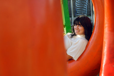 portrait in profile of young latin woman, smiling sitting on a donuts shaped chair in the park, with copy space, she is looking at the camera and smiling.の写真素材