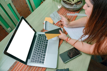 top view of young hispanic latin woman designer working at home looking at wood samples in front of the laptop, leaning on the table, making a decision.の写真素材