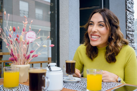 young latin woman of argentinian ethnicity, sitting outside the cafeteria laughing chatting with...