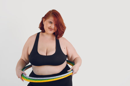 young plus size argentinian latin woman with hula hoops on her waist standing over white background smiling and looking at the camera, people concept, copy space, sporty lifestyle.の写真素材