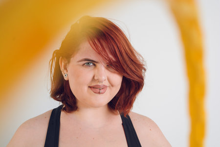 closeup portrait of young plus size argentinian latina woman with green eyes and red hair smiling looking at the camera and with colored earrings around her.の写真素材