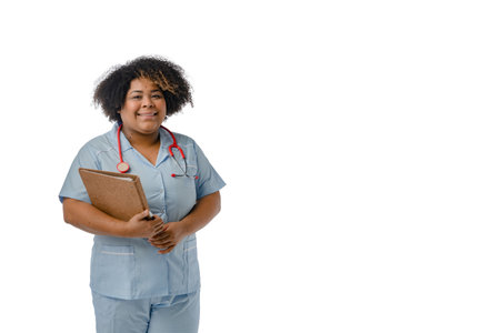 Afro-Latina female doctor of Venezuelan ethnicity in a blue uniform with a red stethoscope over her neck, smiling looking at the camera and holding an open brown folder, white background with copy space.の写真素材