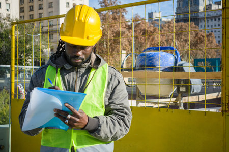 young black man of african ethnicity, wearing green vest jacket and yellow safety helmet,...