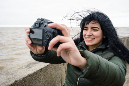 young latin venezuelan woman traveler on the pier next to the river in Buenos Aires, smiling very happy taking a selfie photo with a digital DSRL cameraの写真素材