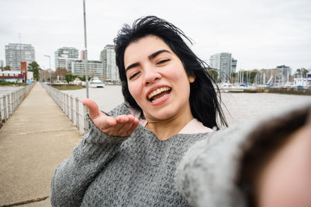 Selfie portrait of young black haired latina woman, wearing a gray sweater, smiling happy looking at...