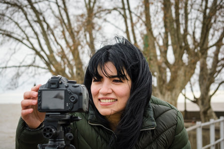 young latin traveler woman outdoors standing adjusting her camera to make vlog video for her social media.の写真素材