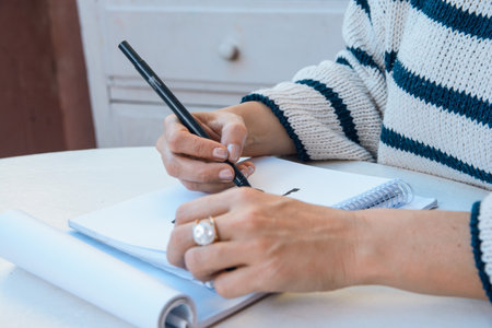 closeup of unrecognizable caucasian female hands with black marker drawing on white paper, sitting...