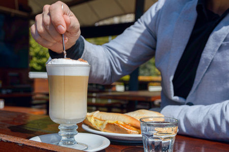 Close-up irreconcilable Caucasian man sitting outside restaurant, stirring mixing cappuccino foam with spoon, food and drink concept, copy space.の写真素材
