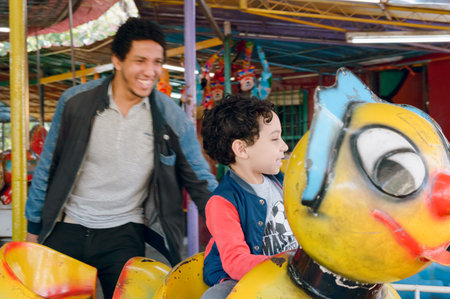 happy latin afro young father watching his son playing on electric worm inside park, focus on child, lifestyle concept. copy space.の写真素材