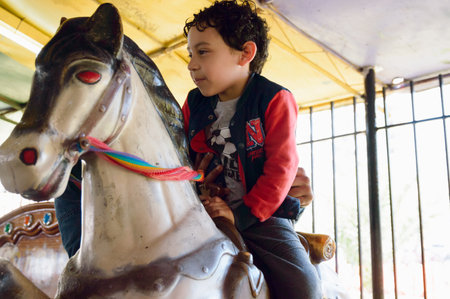 Venezuelan Latino male child, happy riding on pretend horse with his dad at carousel fair, family concept, copy space.の写真素材