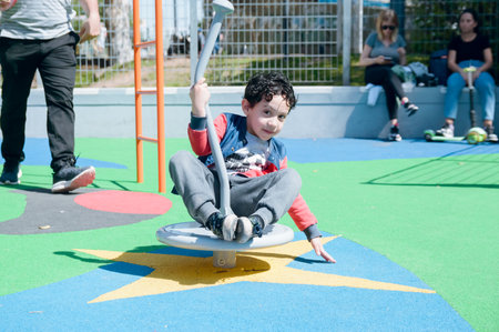 happy and entertaining young Afro Latin Venezuelan boy sitting on playground, playing in park at noon, copy space.の写真素材