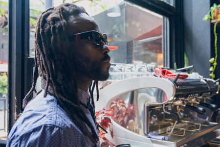 young man of African ethnicity with dreadlocks, beard and glasses, calm standing at restaurant counter looking at menu on wall and thinking what to order for breakfastの写真素材