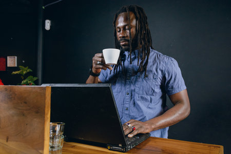 black man of African ethnicity, with dreadlocks and casual clothes, standing working with his...