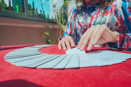 Caucasian Argentinian woman tarot reader, sitting taking card from fan-shaped deck on table,...