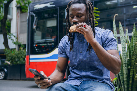 young black african man with dreadlocks and beard, is sitting using mobile and checking phone and...