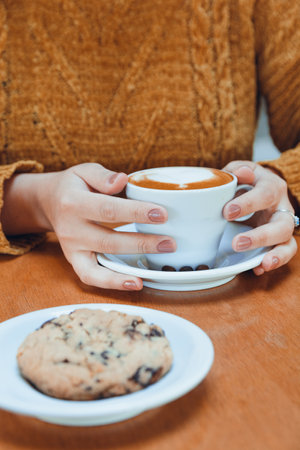 vertical image of unrecognizable woman sitting in cafeteria having snack with cup of coffee and cookie on table, copy space, restaurant concept.の写真素材