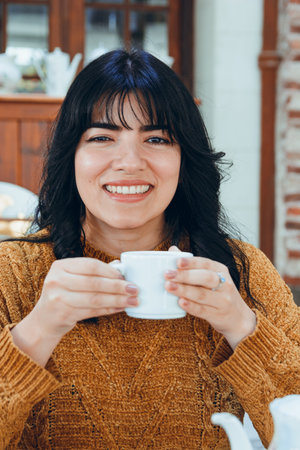 vertical image of young Venezuelan Latin woman, out for walk in Buenos Aires, sitting in restaurant happy drinking tea looking at camera, lifestyle concept, copy spaceの写真素材