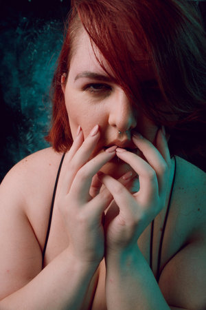 Vertical artistic portrait for social networks, of plus size young Latina woman with red hair and white hair, with natural makeup, she is posing looking at camera with her hands on her faceの写真素材