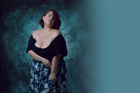 young Latina woman of Argentine ethnicity and white skin, overweight, with short red hair, wearing black shirt and blue skirt with white flowers, standing with artistic backgroundの写真素材