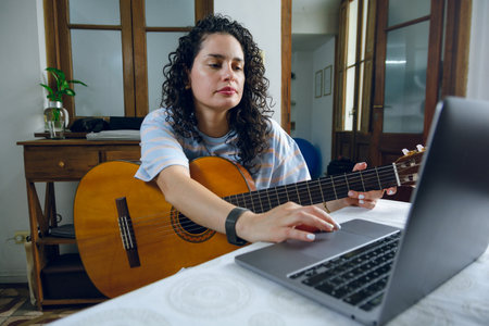 young Latin Venezuelan woman with curlers, calmly sitting with her acoustic guitar at home searching...