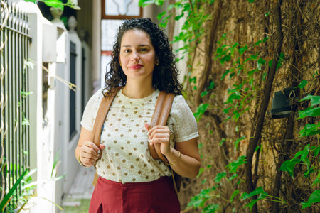 portrait of beautiful young Venezuelan business woman with curlers, carrying backpack and standing...