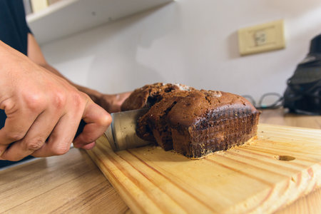 close-up of male hands in kitchen at home cutting sponge cake on cutting board with large steel...