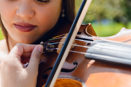 closeup of young latina busker woman violinist tuning violin outdoors before starting work as street performerの写真素材