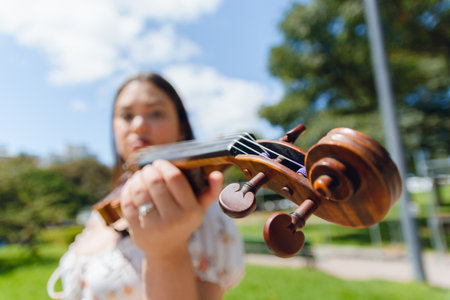 Wide angle portrait of blurred unrecognizable Caucasian woman standing in park holding her violin in street, focus on violin pegs, music concept, copy space.の写真素材