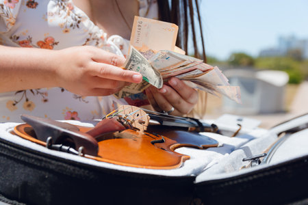 closeup unrecognizable caucasian busker woman counting money with her hands, sitting after working as street artist with her violin, concept of art and money, copy space.の写真素材