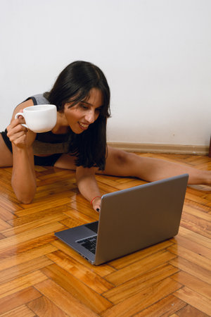 young entrepreneur yoga teacher brunette Argentinian woman, drinking coffee sitting on floor at...