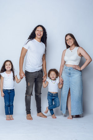 young latin family of father mother and two young girls daughters, having fun posing and smiling, with pants and white flannel, studio shot, white background.の写真素材