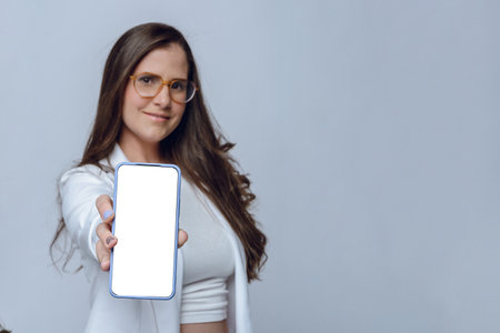 Altina young woman smiling blurred with outstretched hand showing with her hand white screen of phone, focus on phone, studio shot with white background and copy space.の写真素材