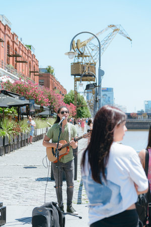 vertical image of young Latino man of Venezuelan ethnicity busker with long hair and glasses,...
