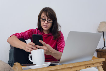 Latin adult woman at home in bed in her bedroom, enjoying her day off watching movies on laptop, she...