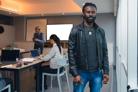 A African Man with dreadlocks and in a black jacket is standing next to the window in the office and...