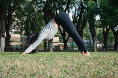 Unrecognizable Woman doing yoga downward facing dog position in park, stretching her hips and...