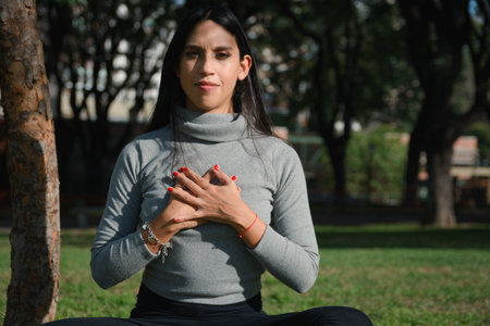 woman sitting in park at sunset with her hands on her chest looking at camera grateful to God for her abundant and prosperous life.の写真素材
