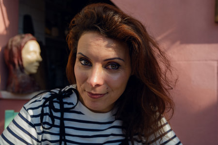 Portrait of a French Caucasian adult Woman, at home wearing a white striped t-shirt, looking at the camera calmly and happily, her face is partially illuminated by the sunの写真素材