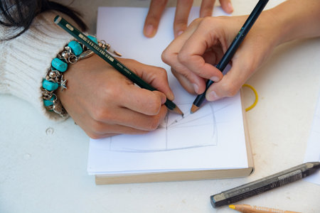 Unrecognizable Multi ethnic female hands drawing lines on a blank sheet of paper, close-up, they are using colored pencils and graphite, education concept, copy spaceの写真素材